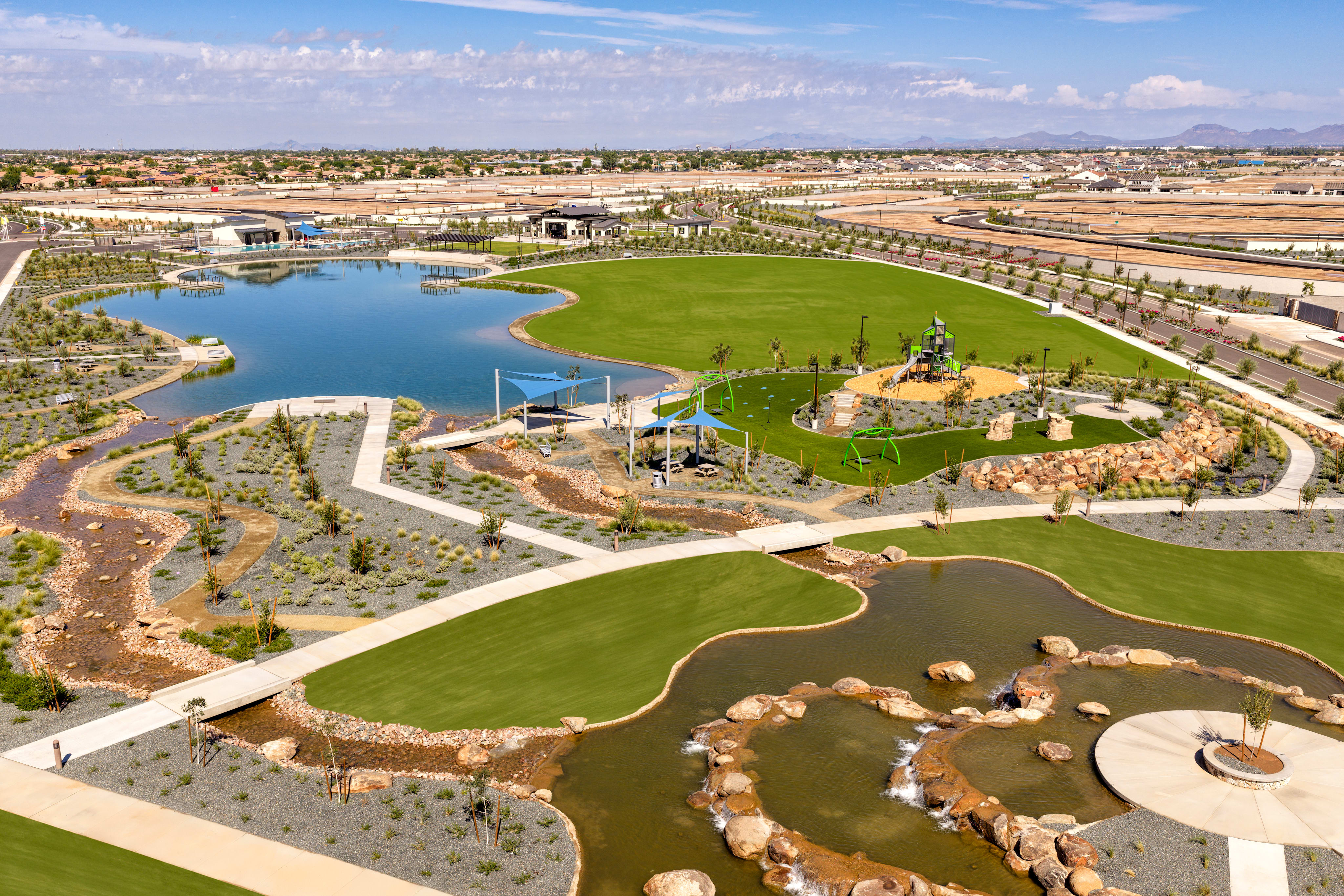 A large, well-manicured golf course with a central lake surrounded by lush greenery, set against a backdrop of residential buildings and a clear blue sky.