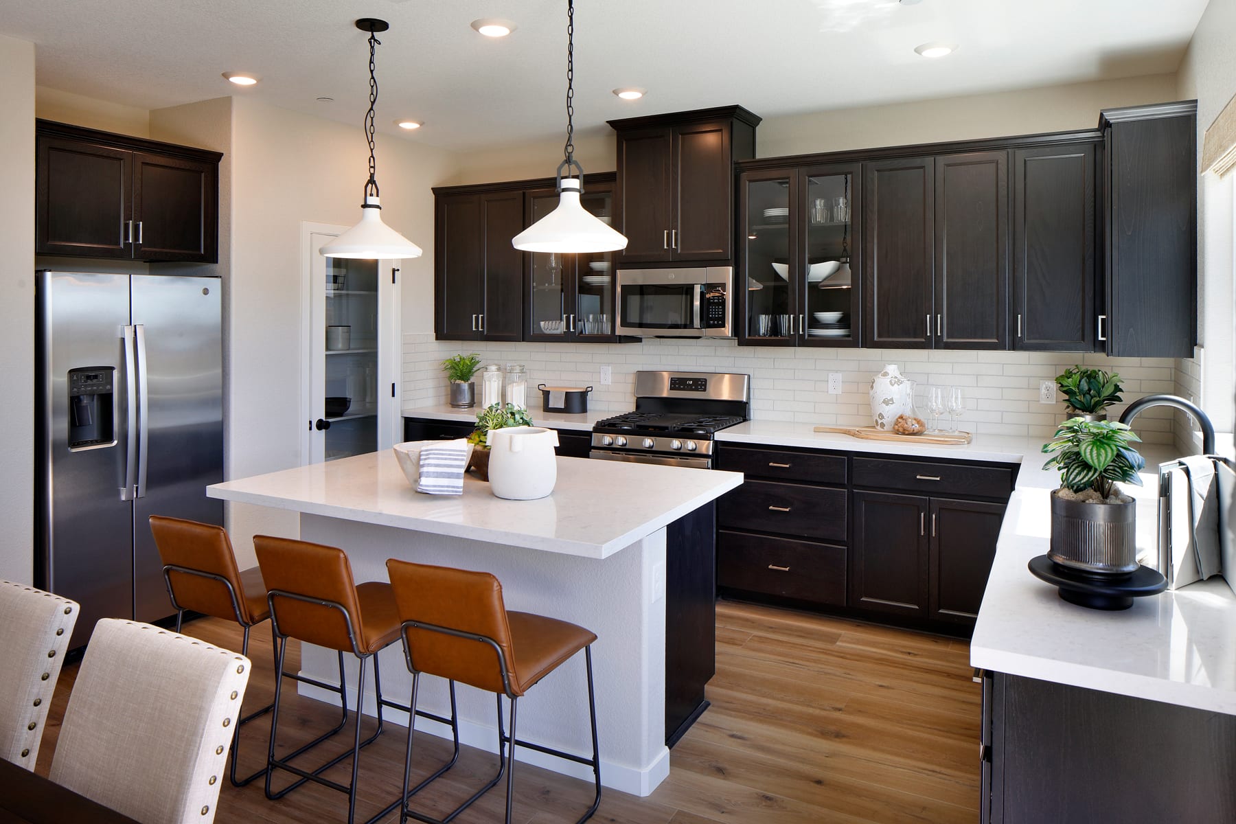 A modern and well-designed kitchen with dark wood cabinets, a white countertop, and pendant lighting over a central island with bar stools.