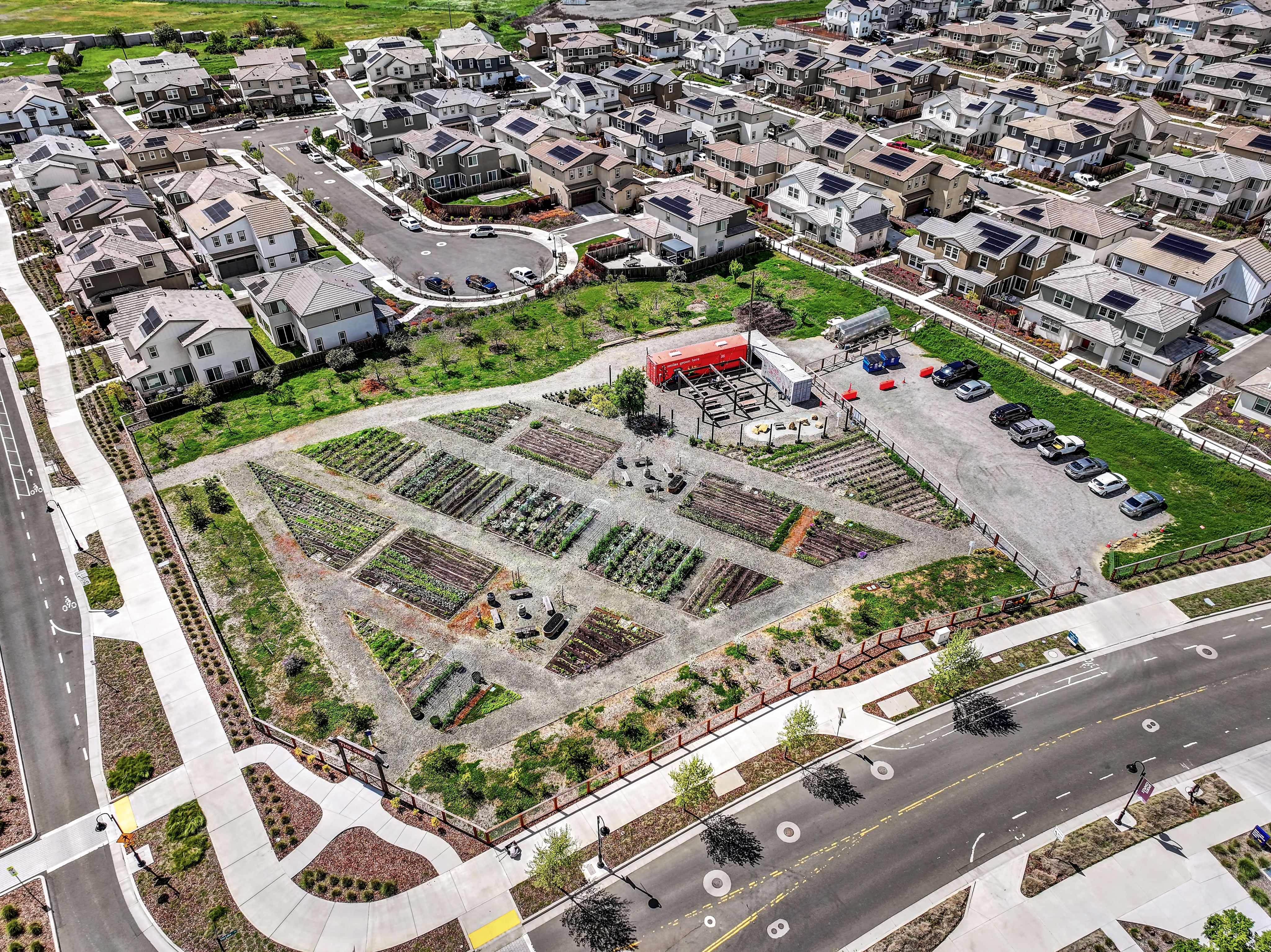 A densely populated residential area with various buildings, roads, and a large community garden or agricultural plot in the foreground.