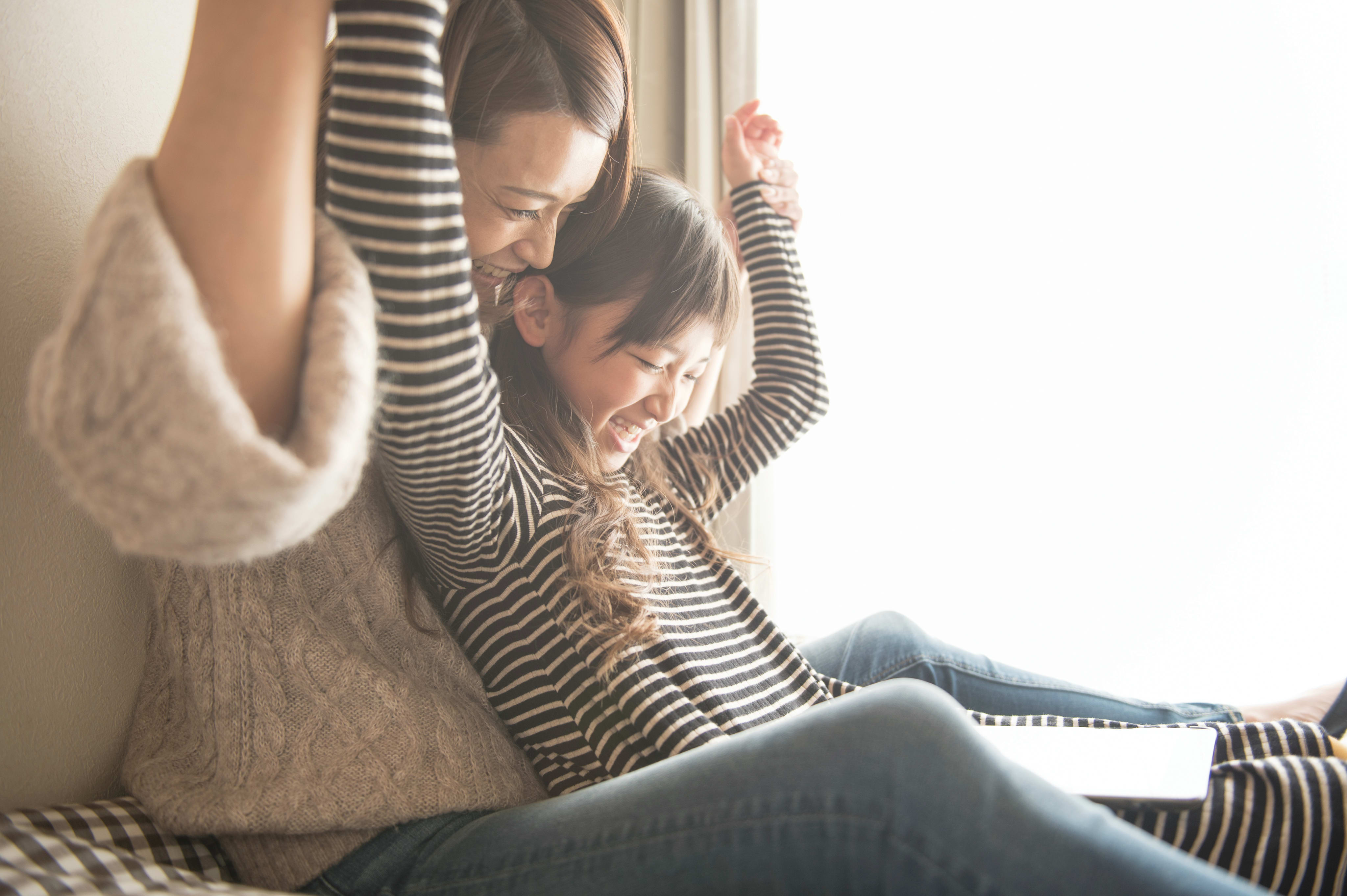 A person in a striped shirt is sitting on a couch, embracing a young child who appears to be sleeping peacefully.