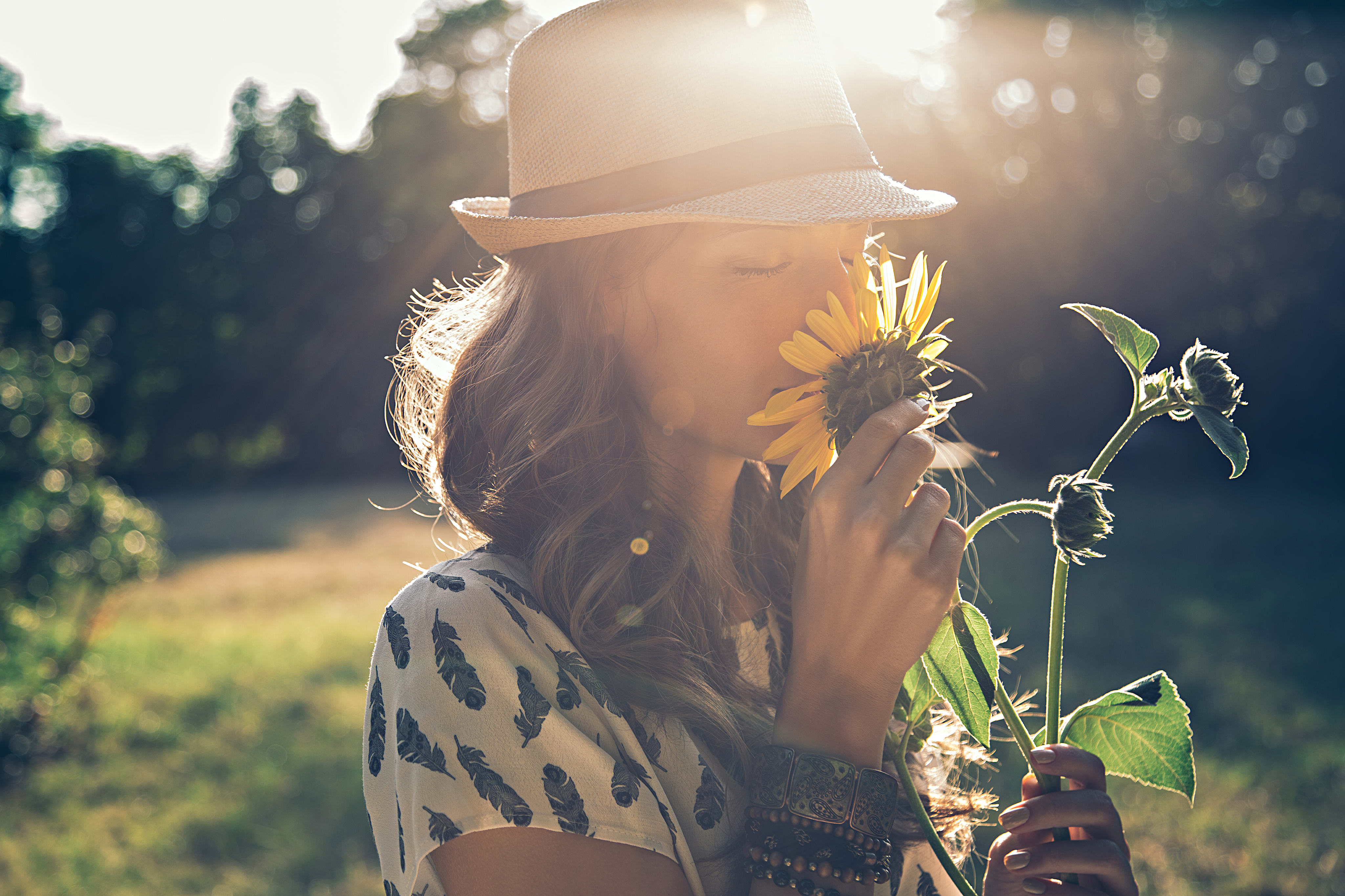 A person wearing a hat and a polka dot shirt stands in a field of sunflowers, with the sun shining brightly in the background.