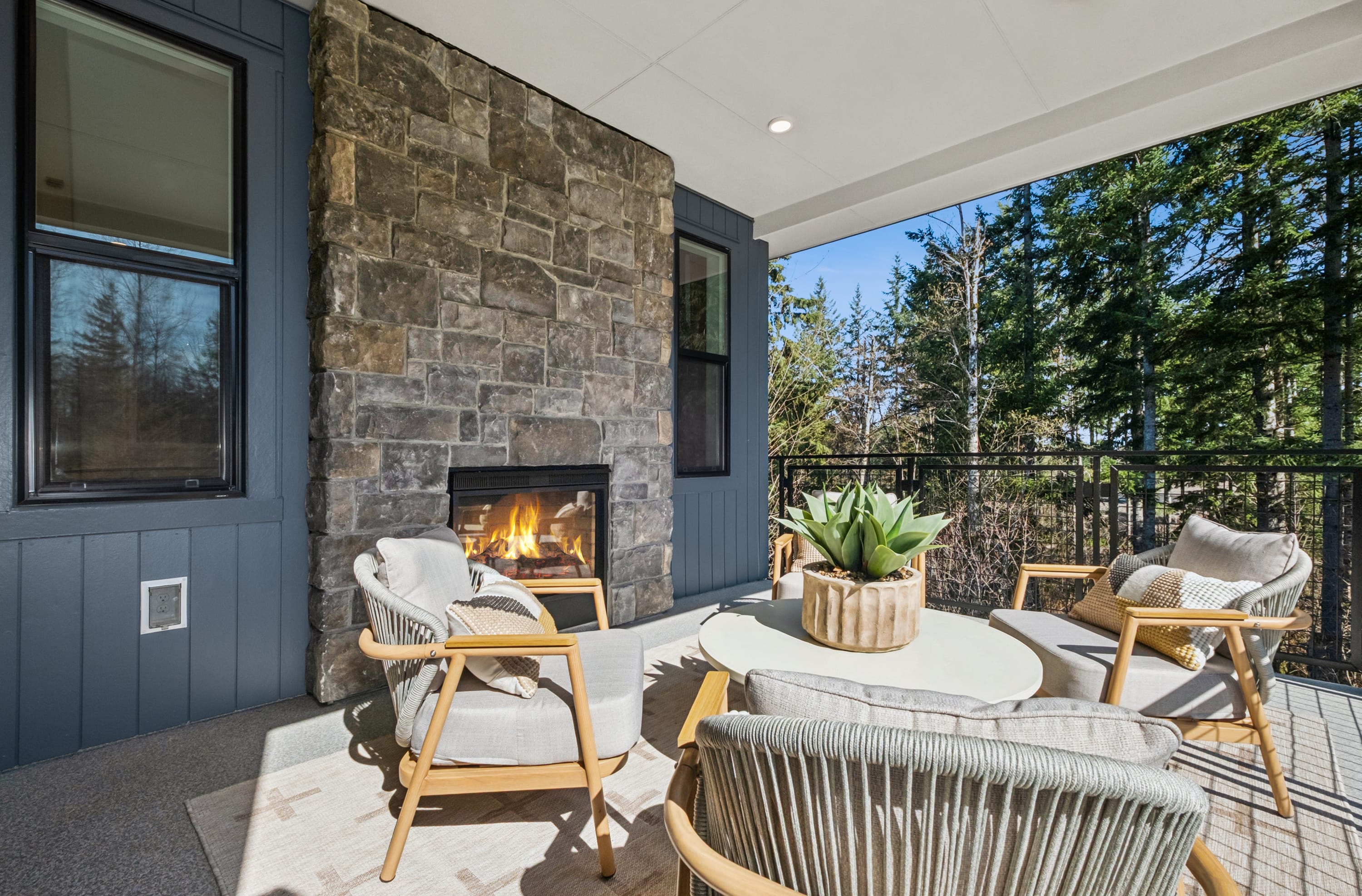 A cozy outdoor living space with a stone fireplace, comfortable seating, and a view of the surrounding trees and nature.
