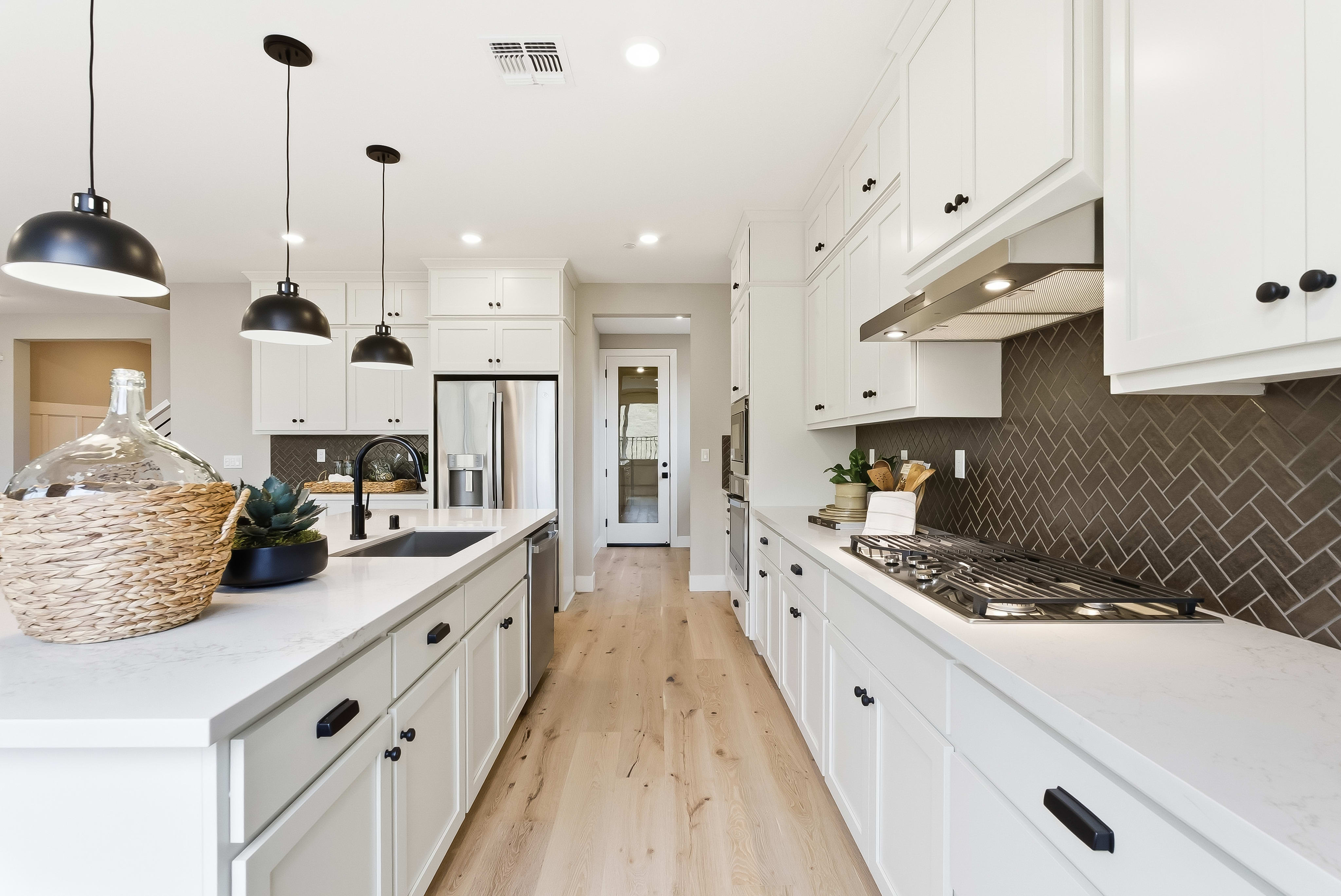 A modern white kitchen with a large island in the foreground and a stainless steel refrigerator and doorway in the background.