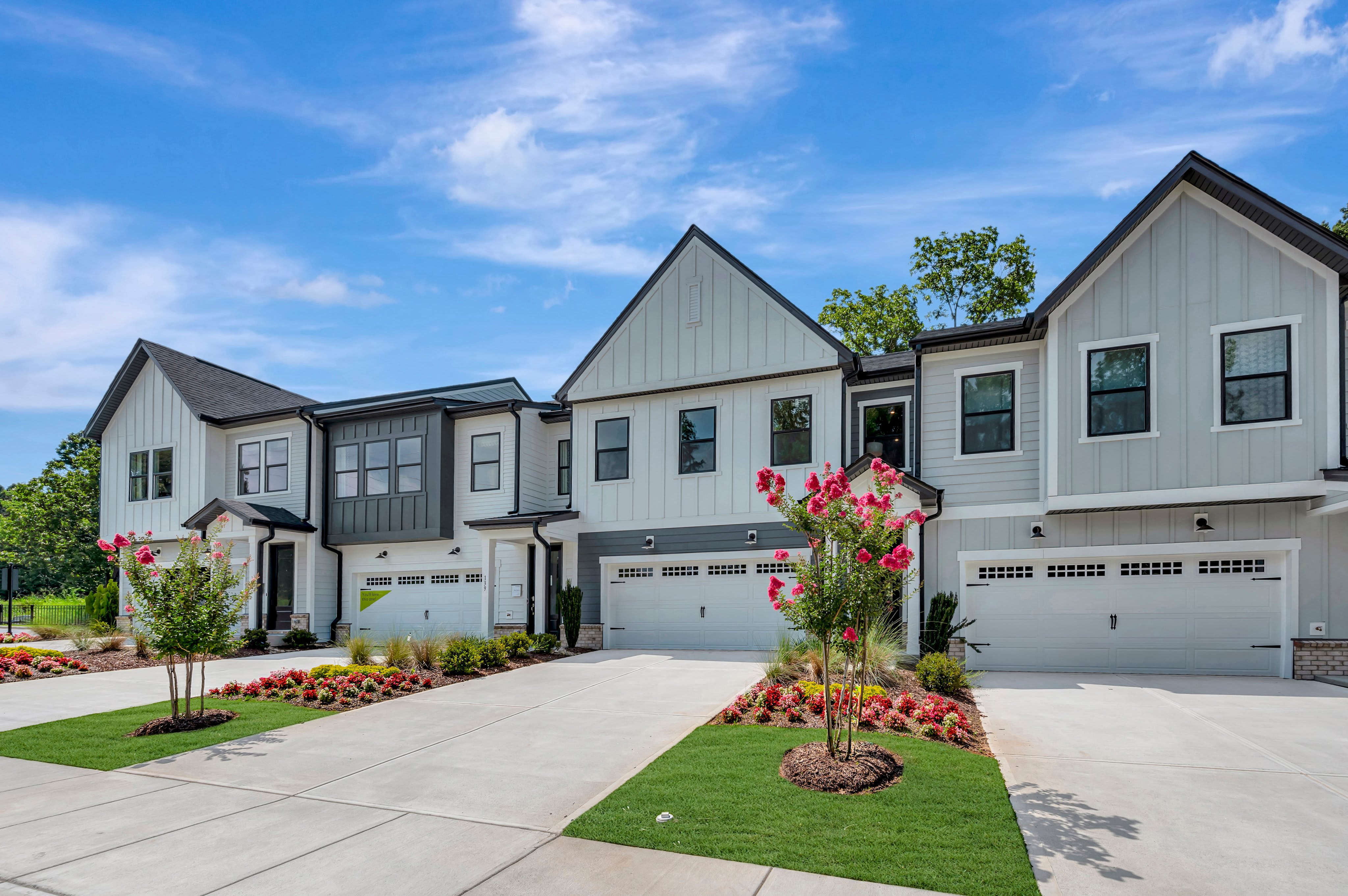 Modern townhouses with manicured landscaping in the foreground stand against a bright blue sky with fluffy clouds.