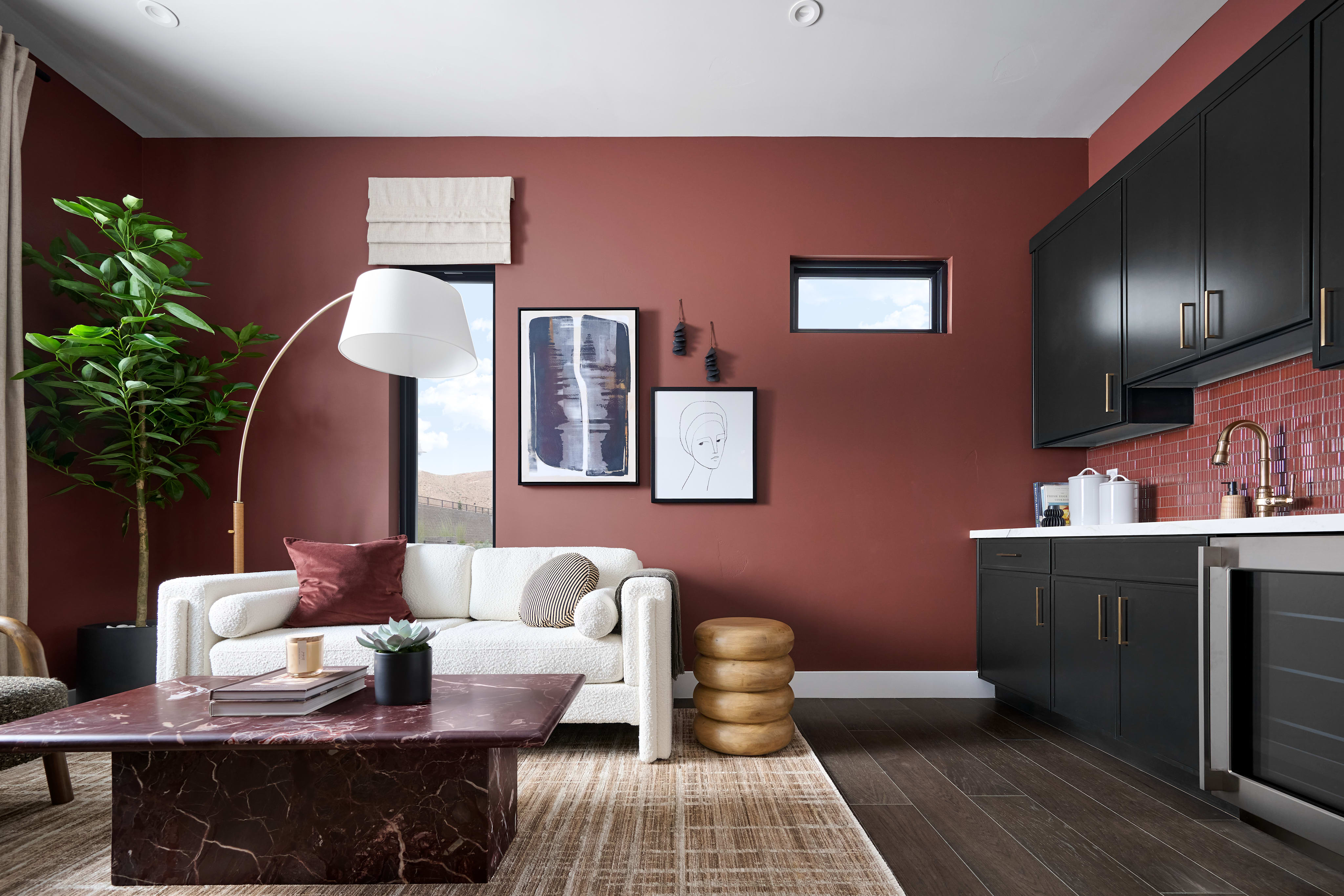 A cozy and stylish living room with a burgundy-colored wall, a white sofa, a wooden coffee table, and various decorative elements such as framed artwork and a potted plant.