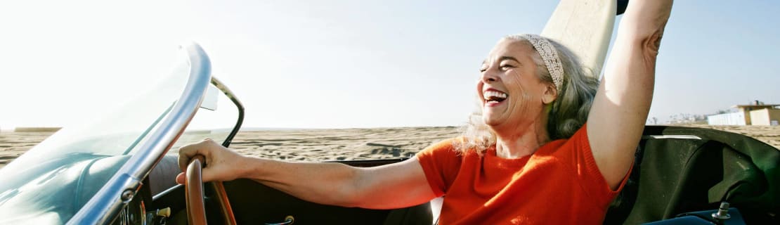 Woman In Convertible Car With Surfboard On Beach