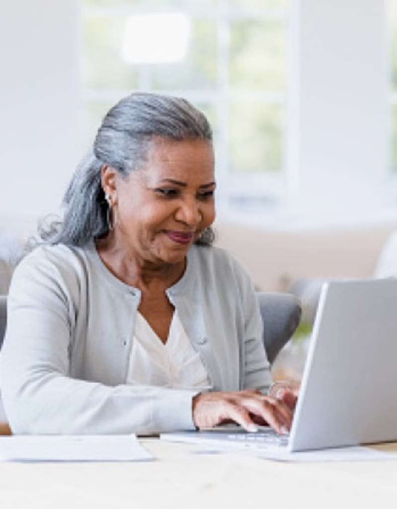 Woman smiling while typing on a laptop, likely comparing Medicare plans.