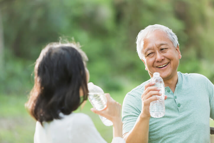 A smiling couple drinks from water bottles after exercise outside