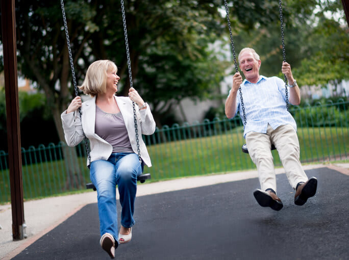 A smiling couple on park swings