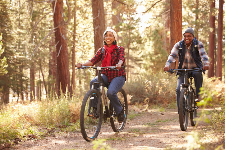 A couple rides bikes through a forest on a sunny day