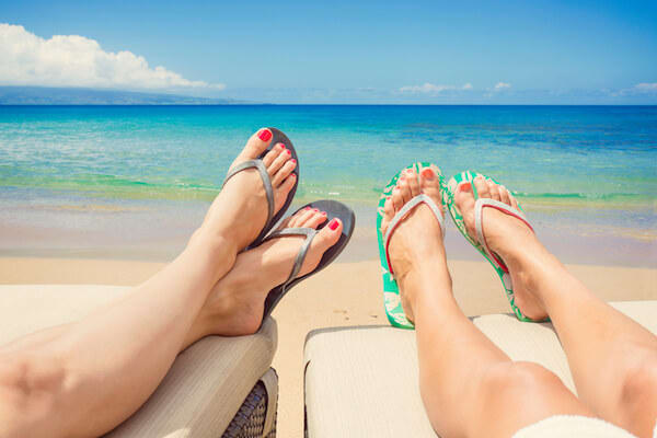 Couples legs in sandals in the sunlight by the beach