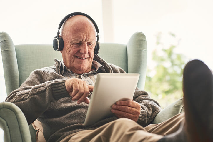 Man sits in chair wearing headphones and using a digital tablet