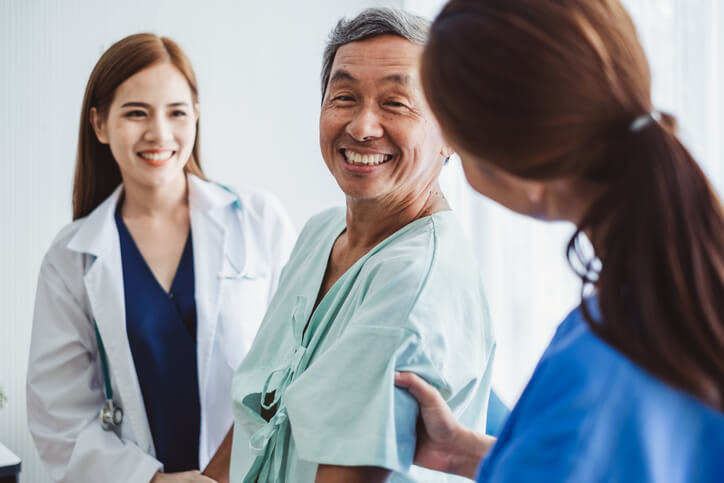 Patient in hospital gown smiles as he speaks with two nurses