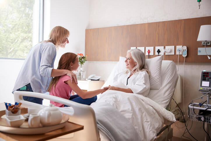 Woman in hospital bed is visited by two women from her family