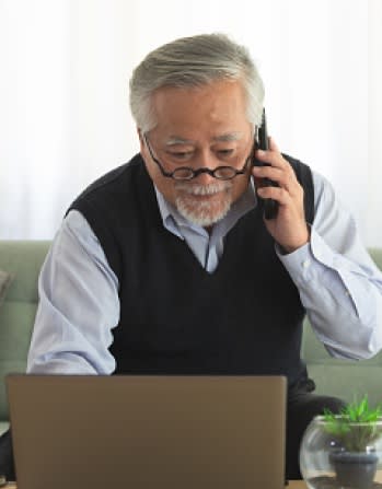 Senior man with glasses on a call, looking at a laptop, discussing Medicare supplements plans on the phone.