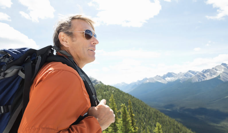 Man wearing sunglasses and a backpack with mountains in the background