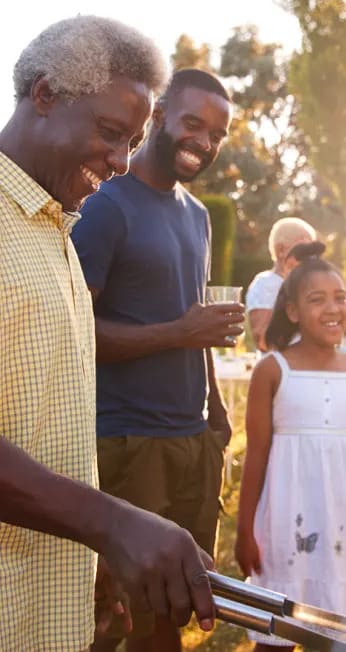 Smiling family gathered outside around a grill