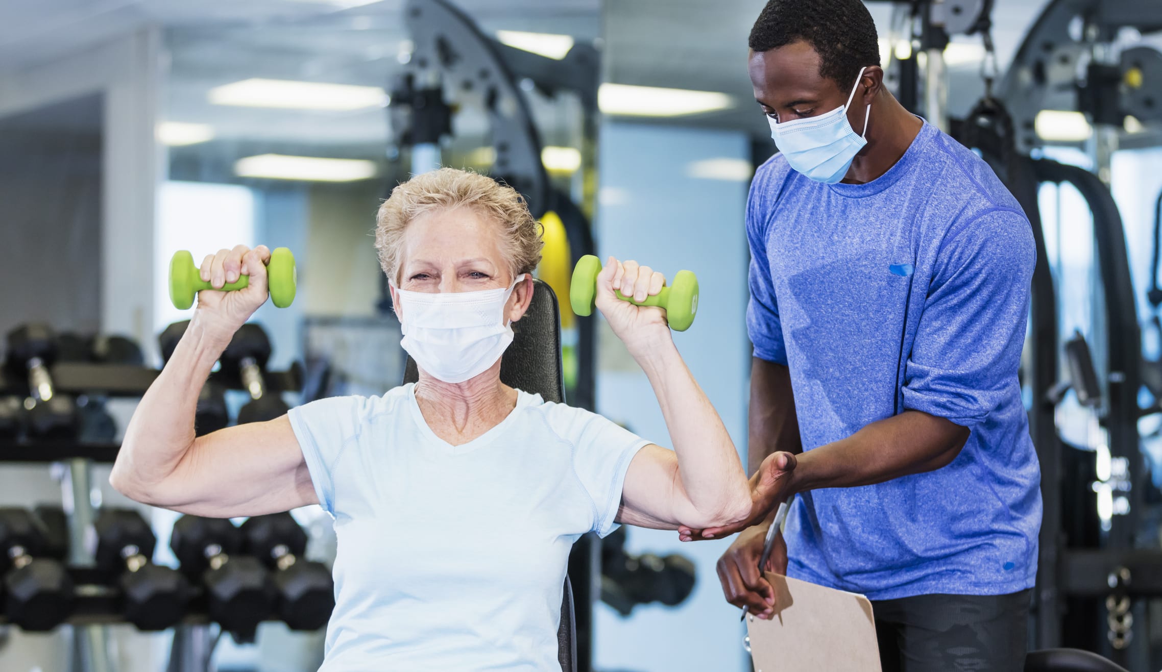 Senior Woman And Personal Trainer In Gym Wearing Masks