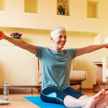 A woman lifts light dumbells while working out on her living room floor at home