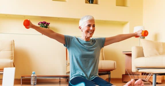 A woman lifts light dumbells while working out on her living room floor at home