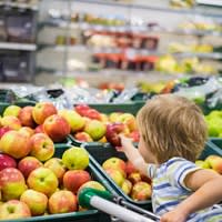 A child reaches for an apple in a grocery store