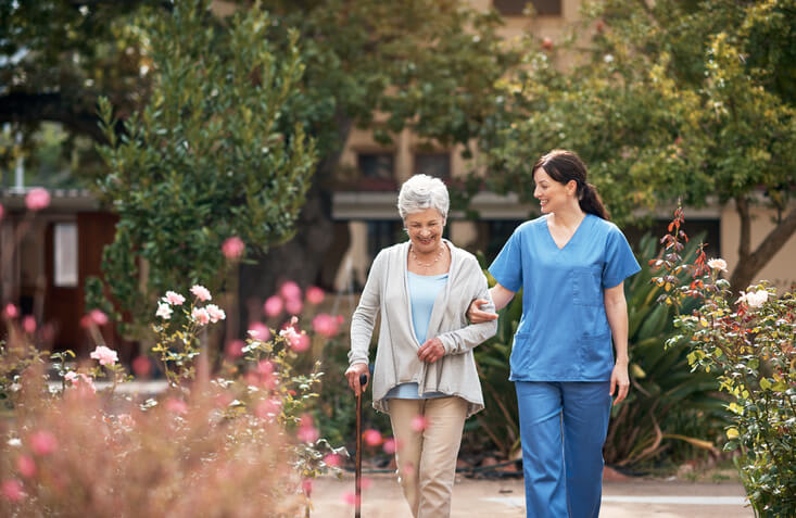 Woman walks in a garden with assistance from caregiver