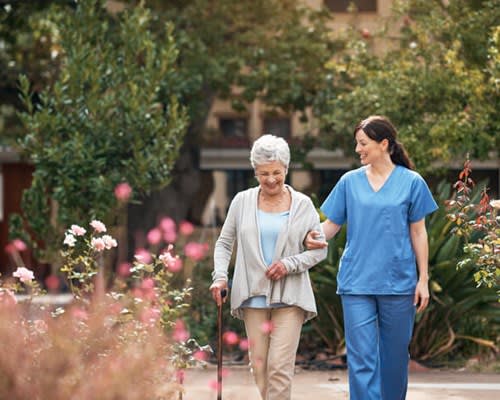 Woman walks in a garden with assistance from caregiver