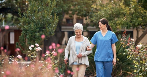 Woman walks in a garden with assistance from caregiver