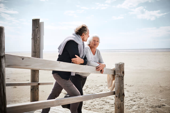 Retired couple leaning on a fence at the beach