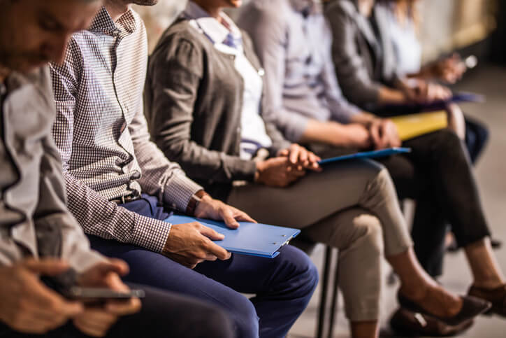 People sitting with resumes and waiting in line for job interviews