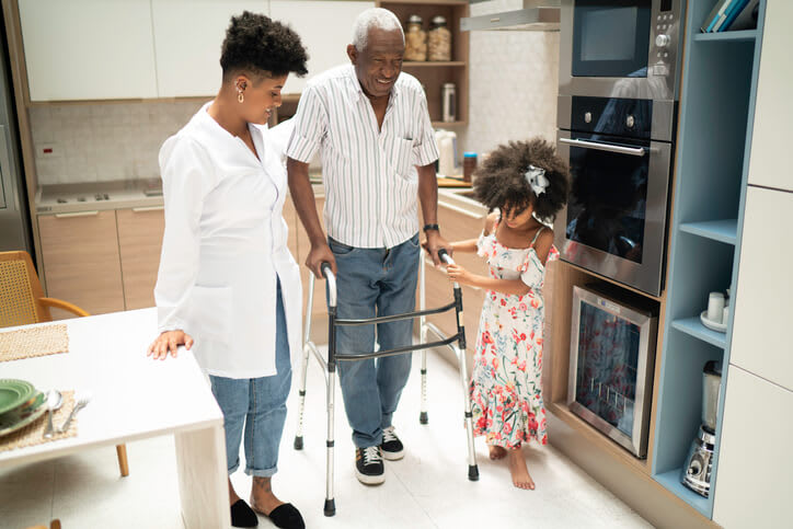 Man assisted while using walker in his kitchen