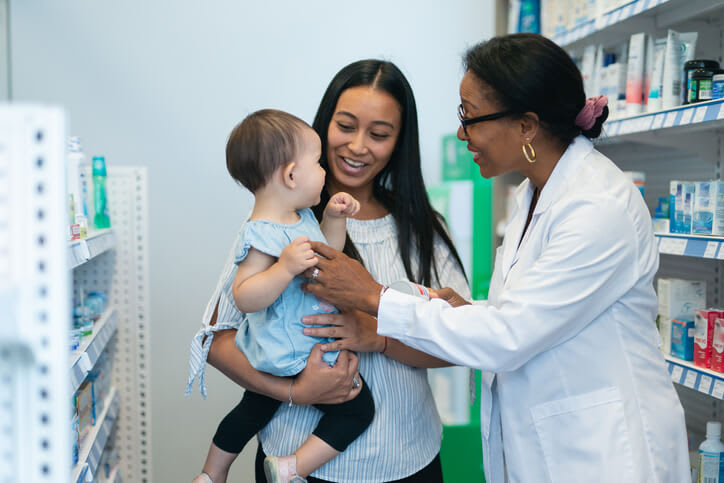 Happy pharmacist speaks with young mother and baby girl