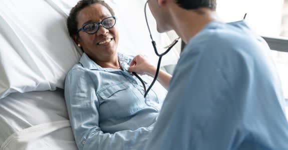 Smiling woman in hospital bed attended by nurse