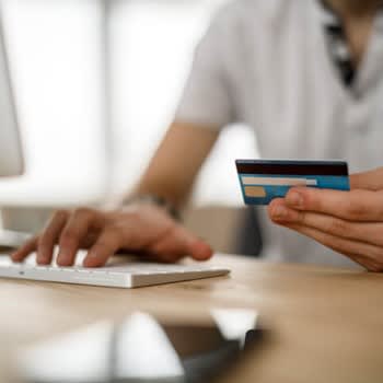 Someone holding credit card while typing on computer