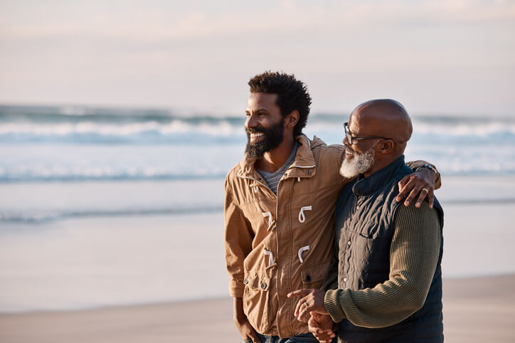 A father and adult son embrace and walk on the beach