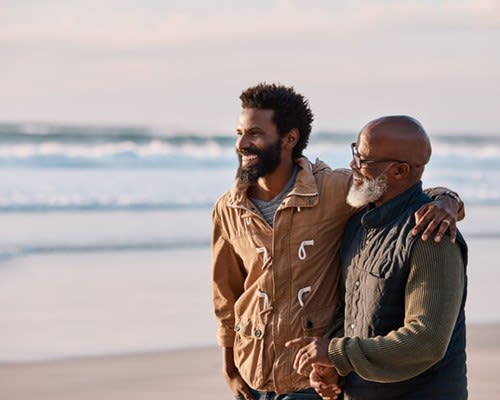 A father and adult son embrace and walk on the beach