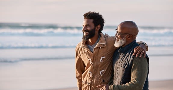 A father and adult son embrace and walk on the beach