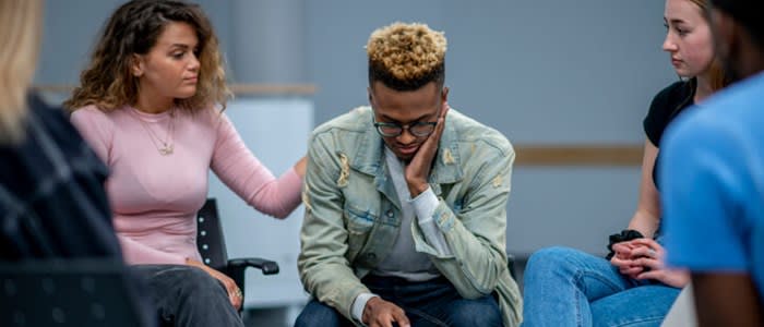 Young woman comforts fellow member of group therapy session