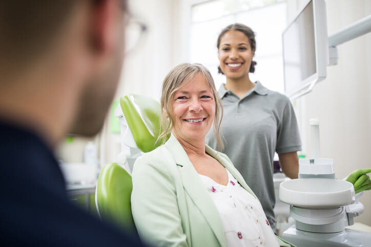 Woman smiles at her dentist with dental assistant in background