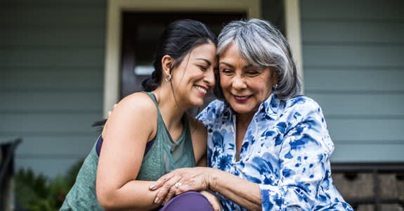 Woman and adult daughter embrace and smile while sitting on home front steps