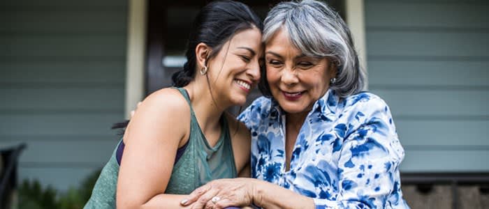 Woman and adult daughter embrace and smile while sitting on home front steps