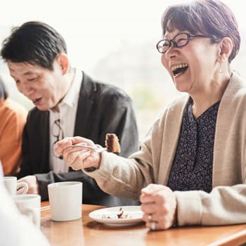 Woman laughs while eating cake and drinking coffee with friends