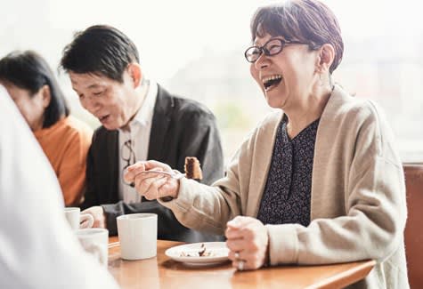 Woman laughs while eating cake and drinking coffee with friends