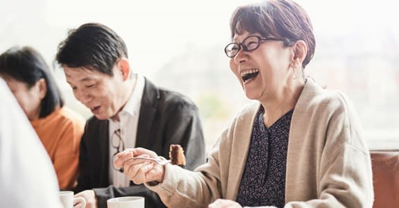 Woman laughs while eating cake and drinking coffee with friends