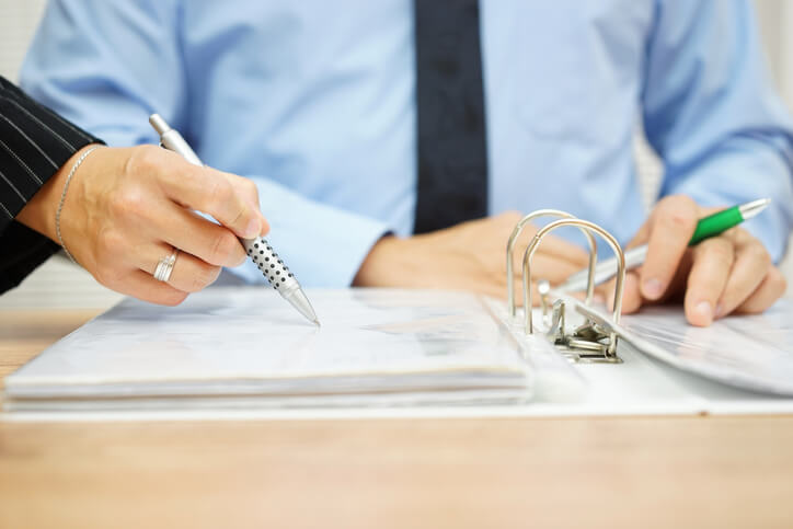 A woman's hand holding a pen points out an item in a binder