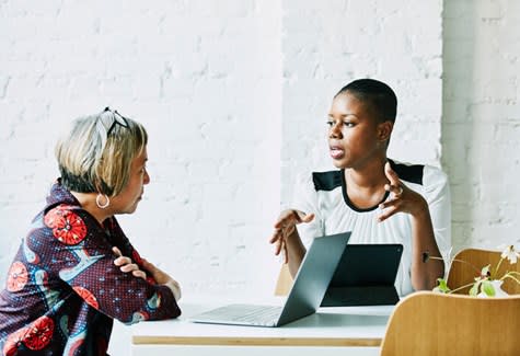 Two women chat while one uses her laptop computer