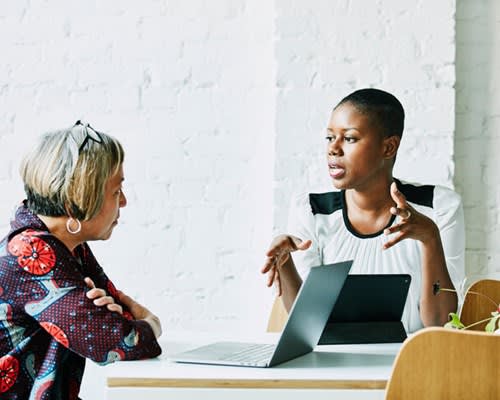 Two women chat while one uses her laptop computer