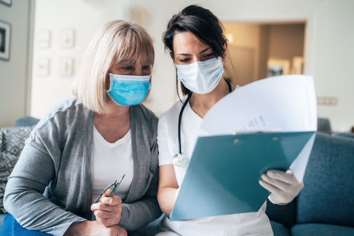 Doctor reviews medical charts with her patient while both wear face masks