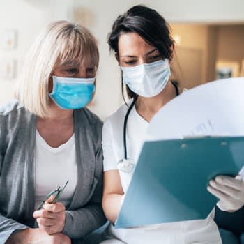 Doctor reviews medical charts with her patient while both wear face masks