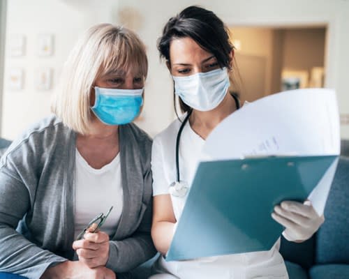 Doctor reviews medical charts with her patient while both wear face masks